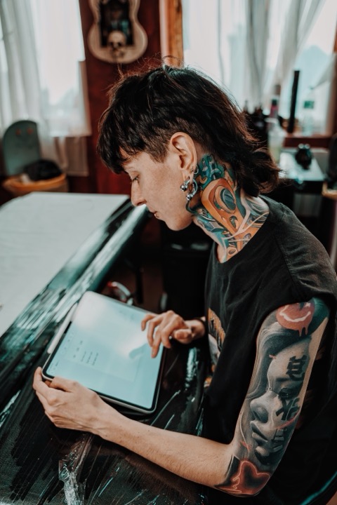 Carlotta Scomazzon at her desk drawing a design on a tablet, her neck and arms covered in colour tattoos.